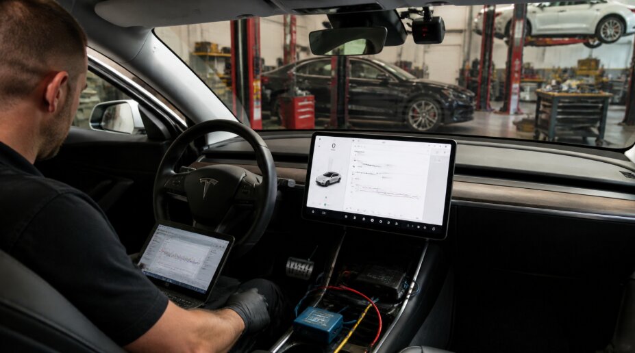 A mechanic calibrating a Tesla ADAS camera in Tigard SUV and Auto Repair. The vehicle's interior screen displays diagnostics while the mechanic monitors the calibration process.