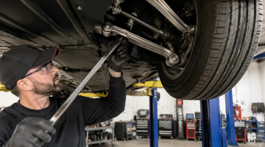 Mechanic inspecting the suspension components of a Tesla Model Y under a hoist inside Tigard SUV and Auto Repair.