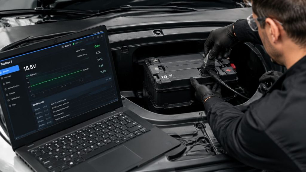 A professional technician performing a 16V Lithium-ion battery health diagnostic on a Tesla Model Y in a Tigard workshop, using a laptop with advanced system analysis software